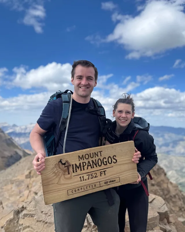 Spencer Hepworth on the summit of Mount Timpanogos, holding the 11,752 ft summit sign
